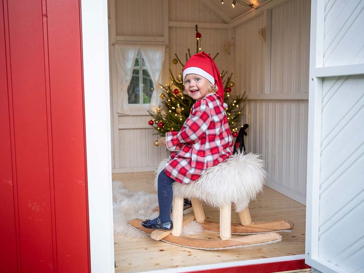 Girl swinging on a toy horse in a red wooden playhouse by WholeWoodPlayhouses