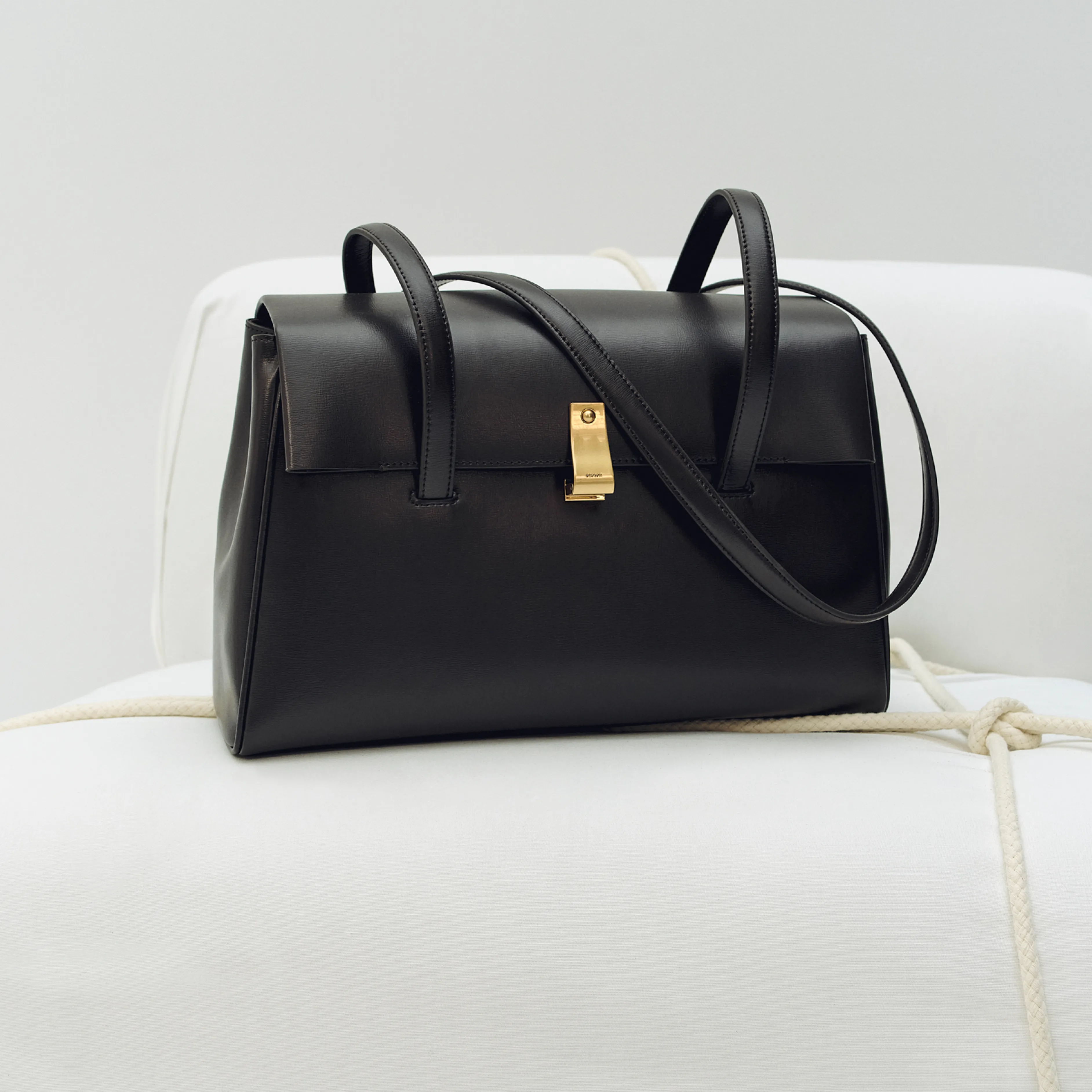 A stylish black handbag with a gold clasp resting on a white surface.