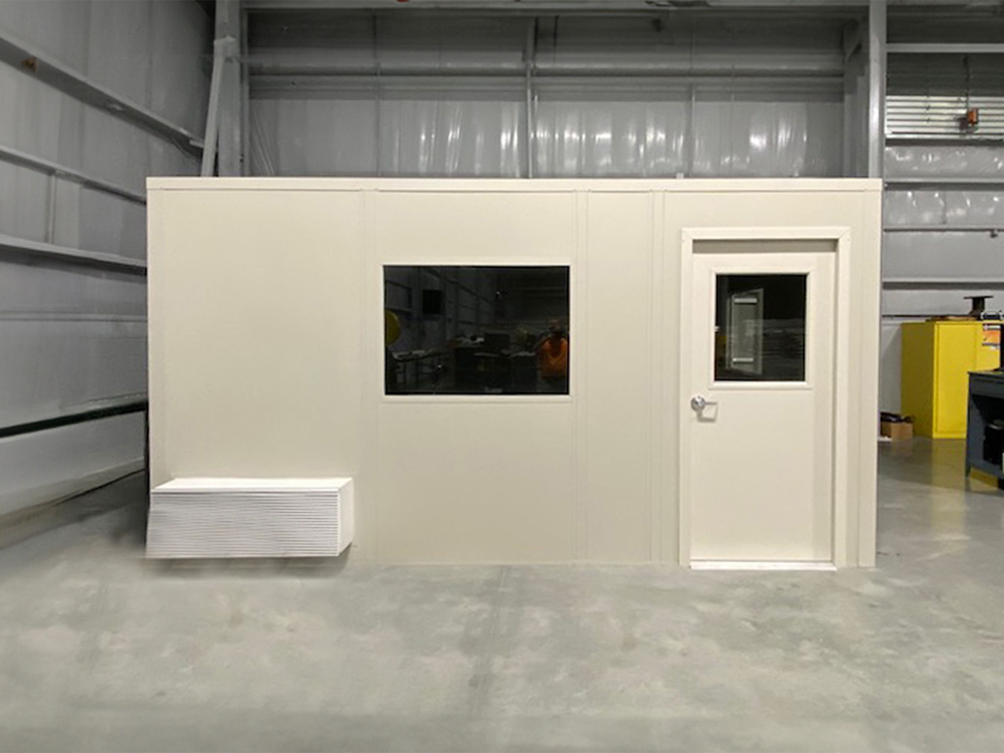 A white modular office with a window and door in a warehouse.