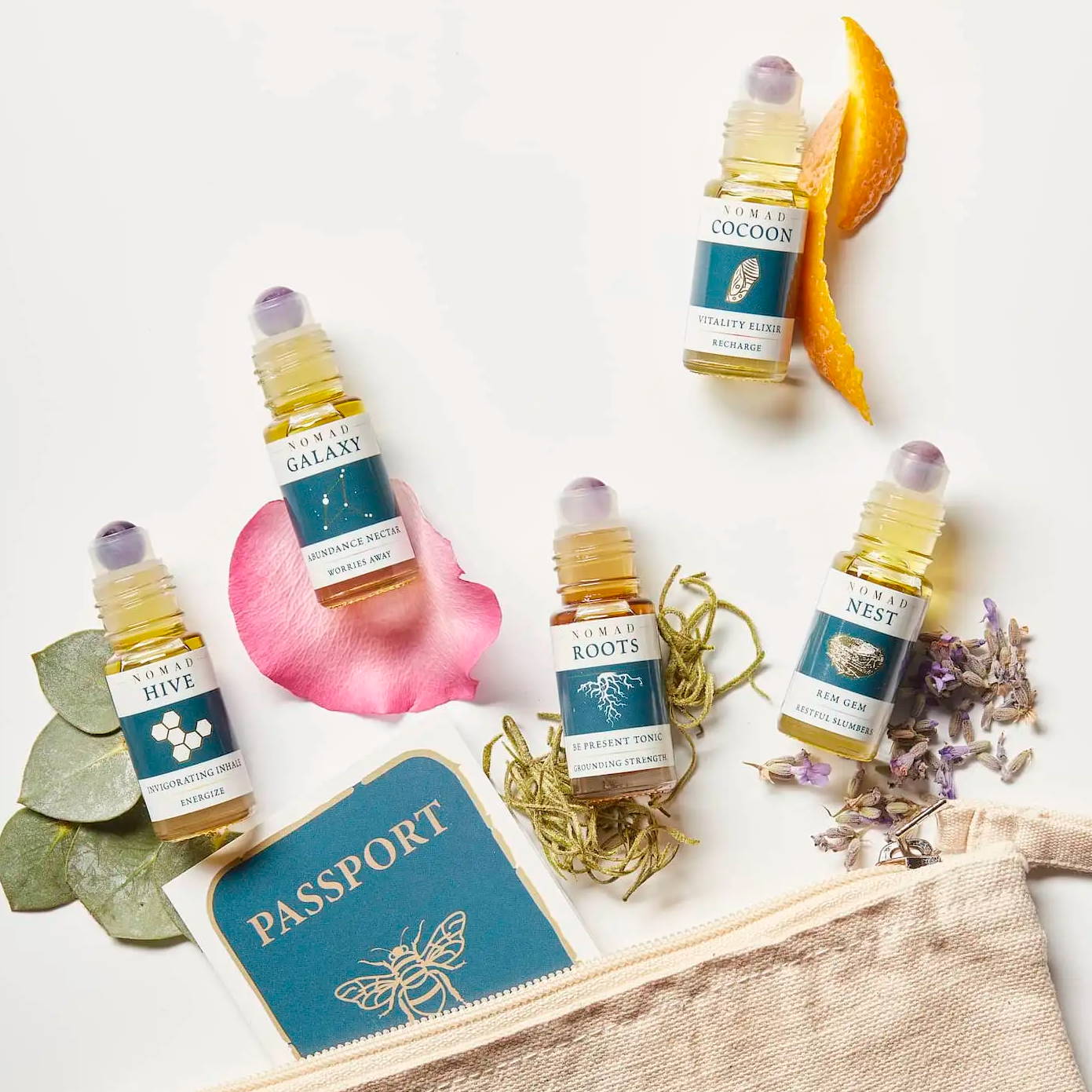 Five aromatherapy blends nested on corresponding botanicals near their travel pouch and passport brochure