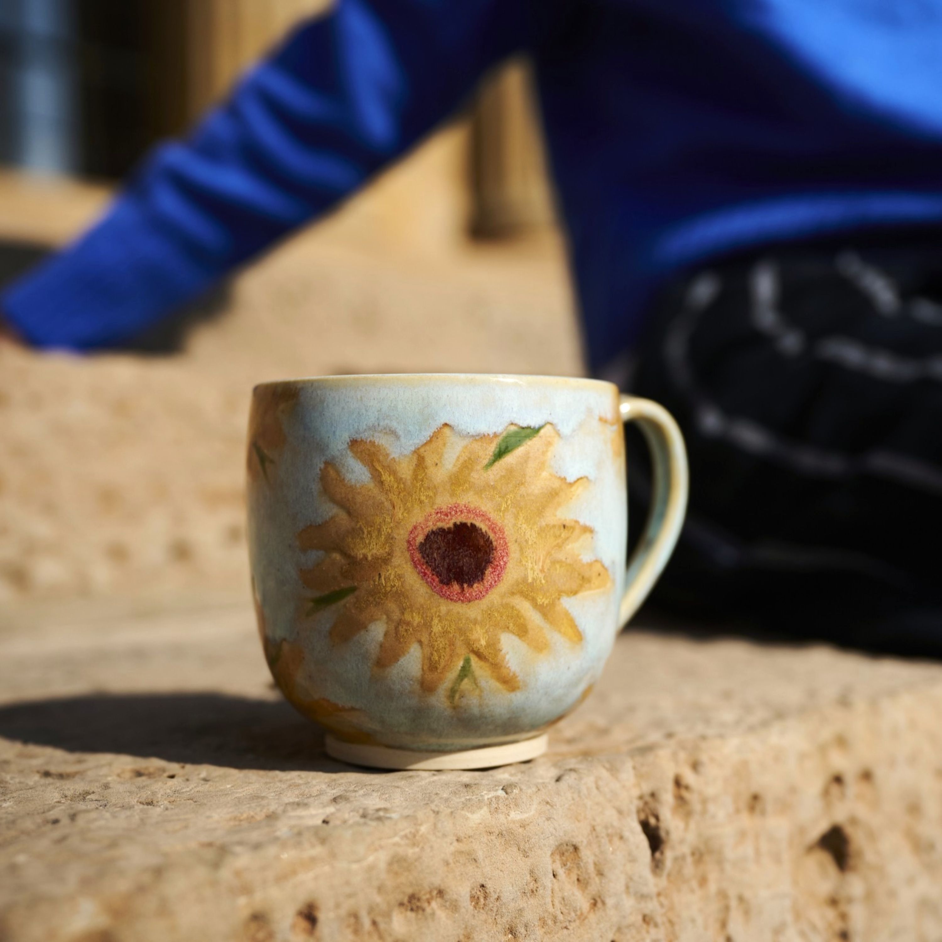 A ceramic mug with a sunflower design on a stone surface.