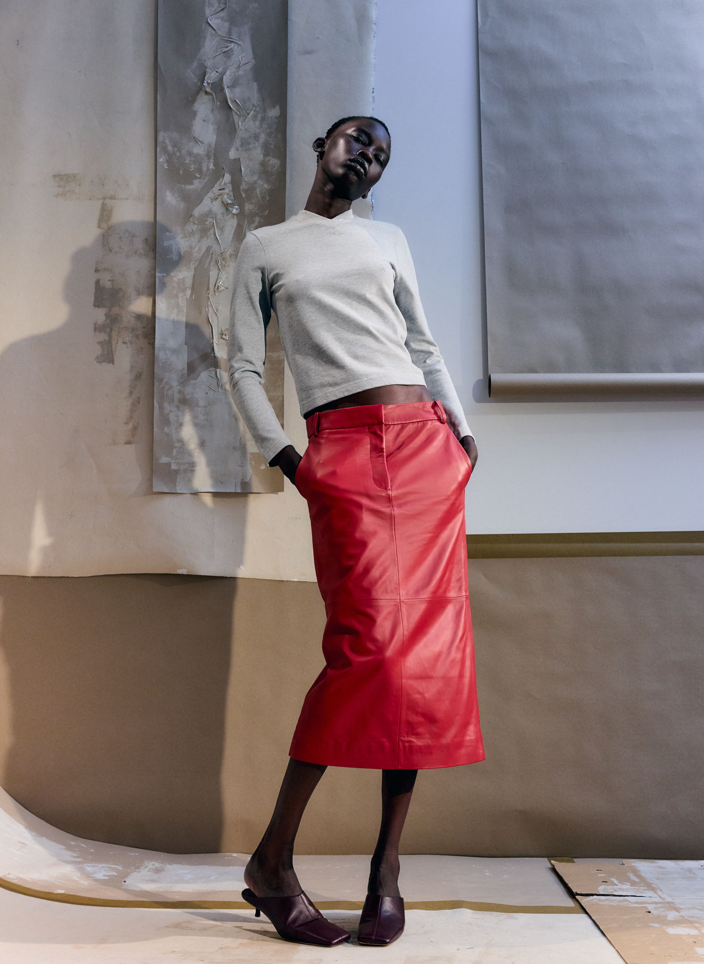 Model wearing a gray sweater and red skirt in an artistic setting.