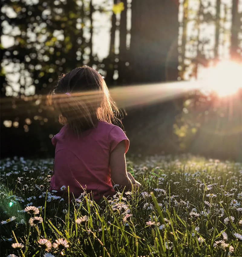 Kleines Mädchen sitzt im Wald im Sommer und schaut auf die Sonne