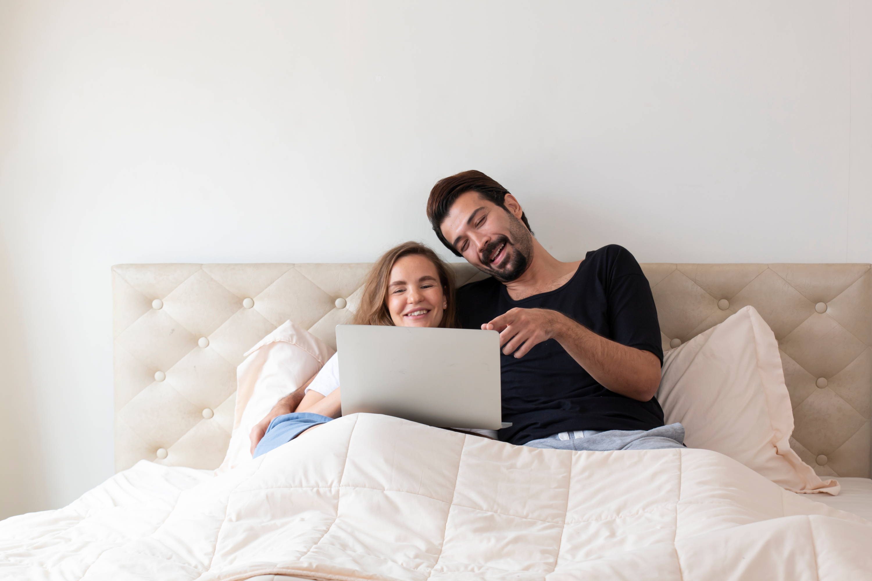 A man and woman lay in bed watching a movie on a laptop together.