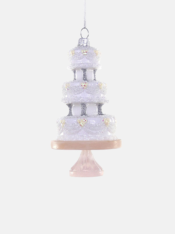 A decorative three-tiered wedding cake ornament with white frosting and a pink base.