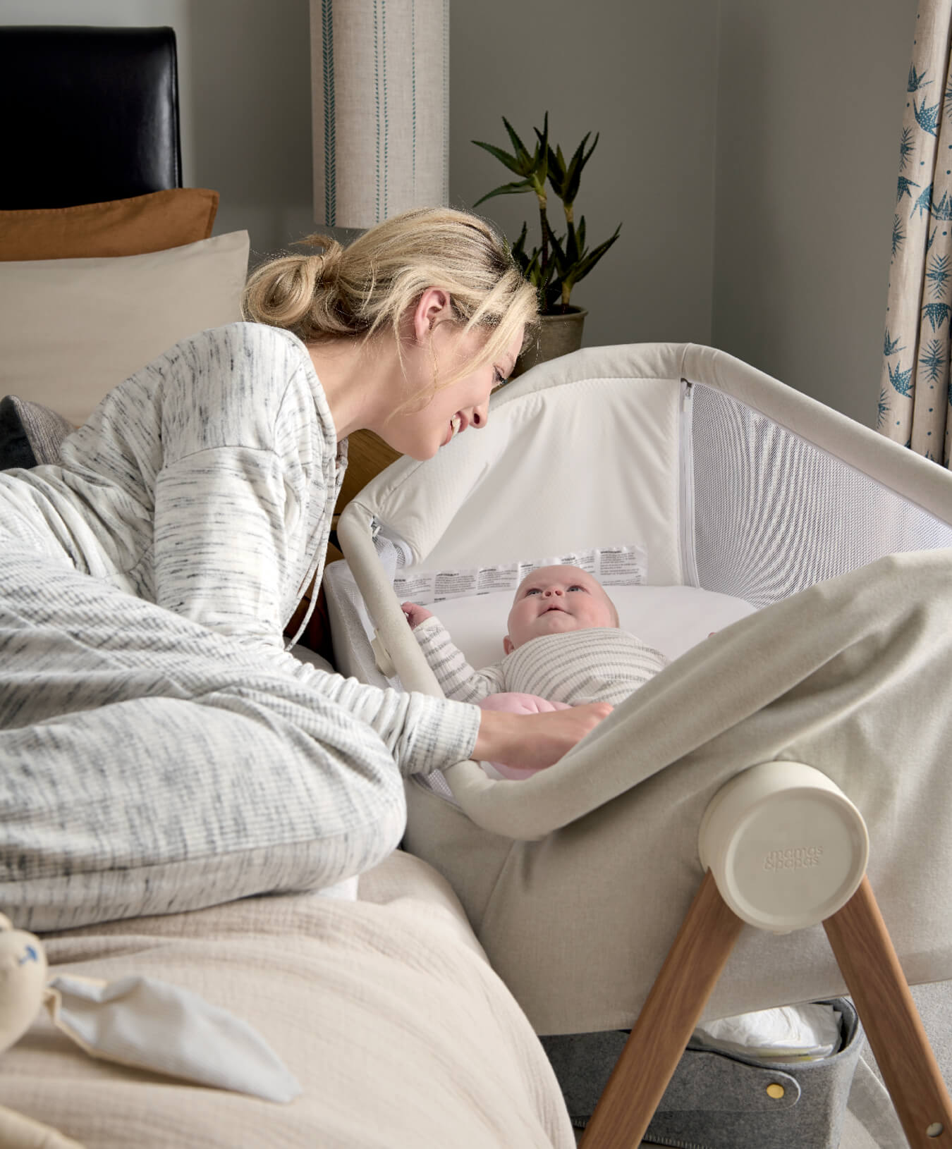 A mother lovingly gazes at her baby in a Lua Fawn Bedside Crib.