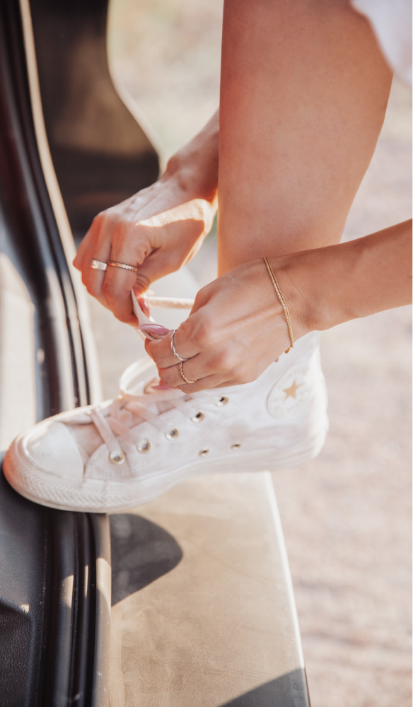 Someone tying the laces on a pair of white Converse sneakers