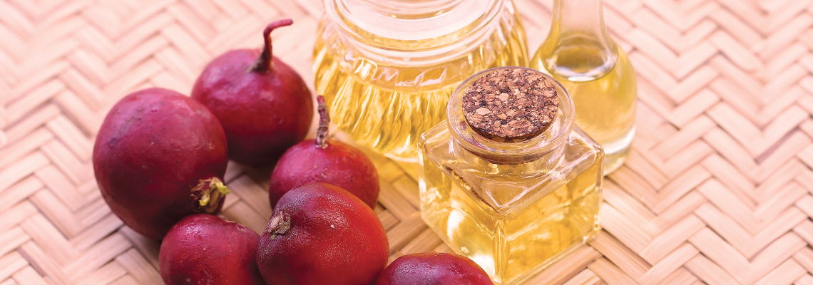 Bottles of oil beside red fruits on a woven surface.