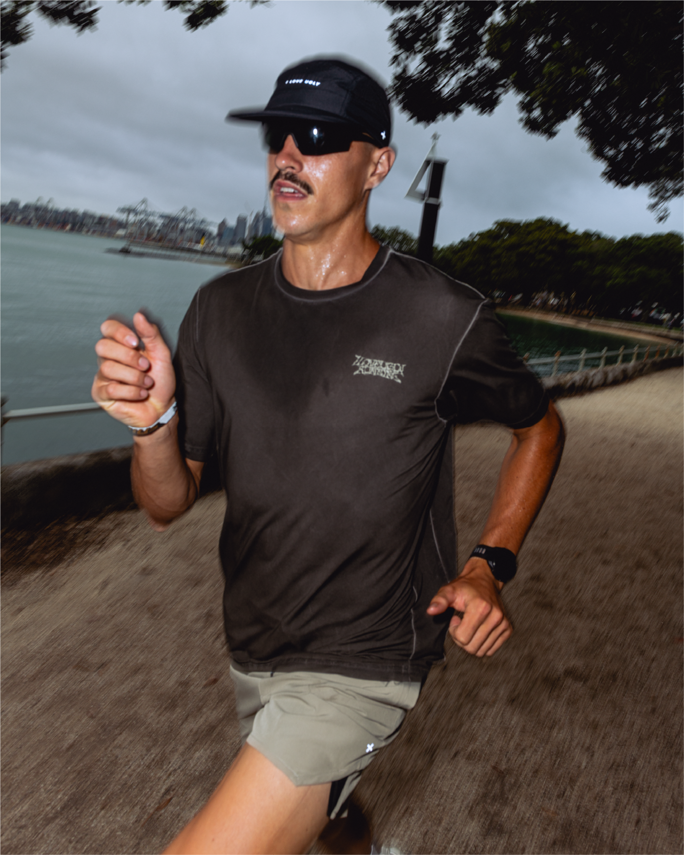 Man running along a path near water, wearing a cap and sunglasses.