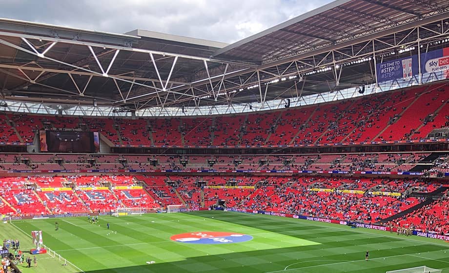 Wembley Stadium with empty seats and a green football pitch.