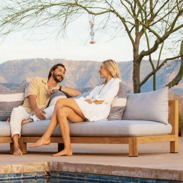Pacific 2-Seat Armless Sofa with a contemporary teak wood frame and white cushions, styled in a minimalist outdoor space beside a pool, perfect for modern patios and summer lounging.
