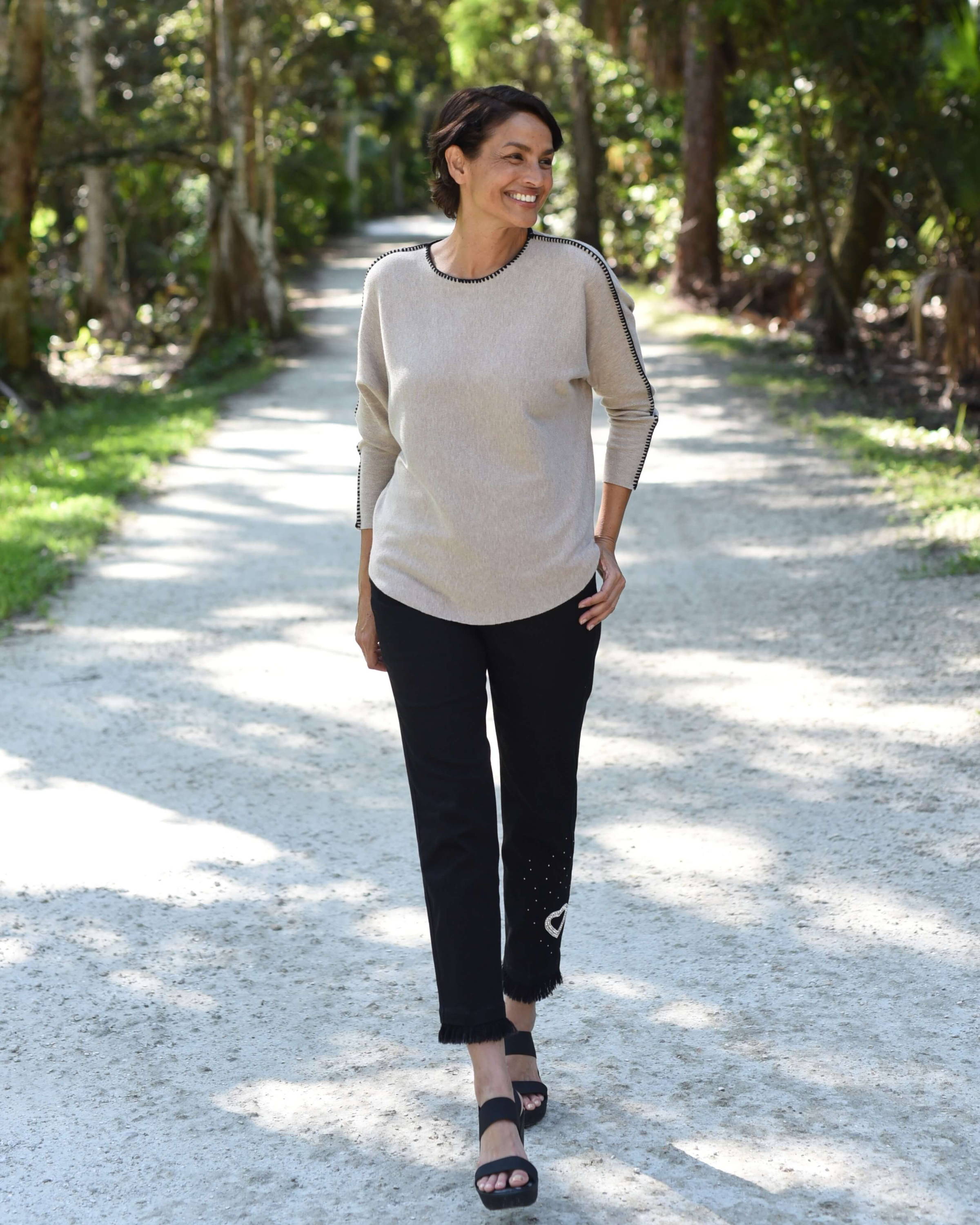 A woman with short dark hair walks down a paved path in a wooded area.