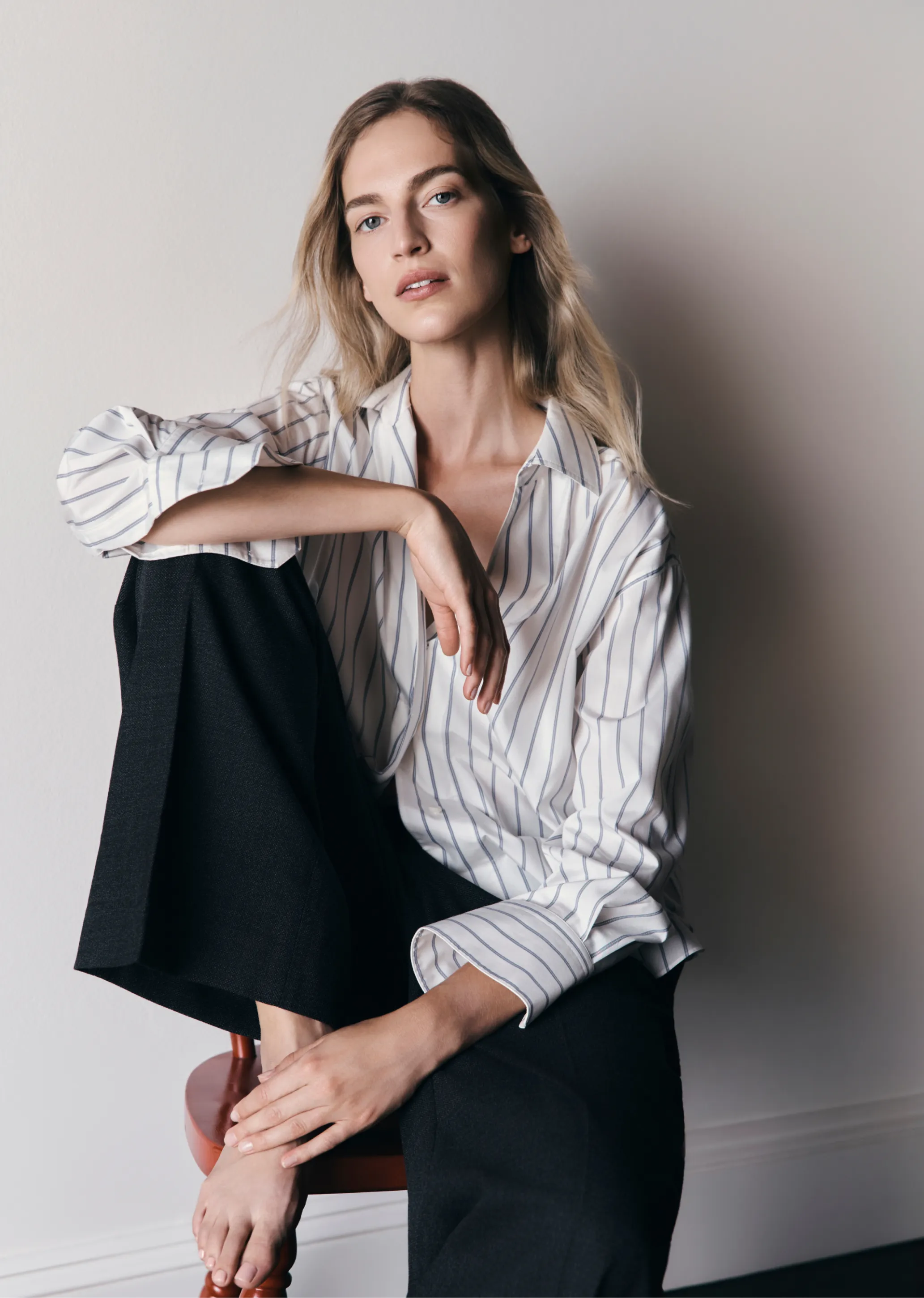 A woman sitting on a chair, wearing a striped shirt and black pants.