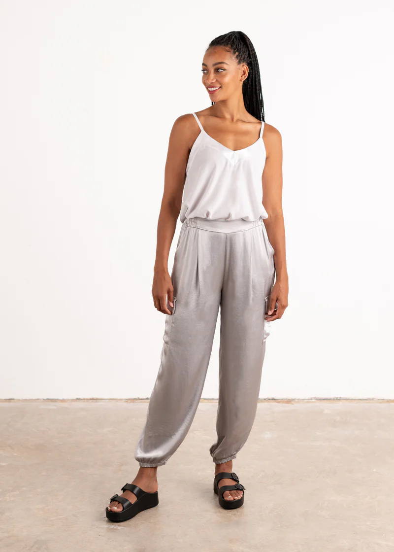 A model  wearing a white sleeveless camisole with silver, satin cargo trousers and black slides