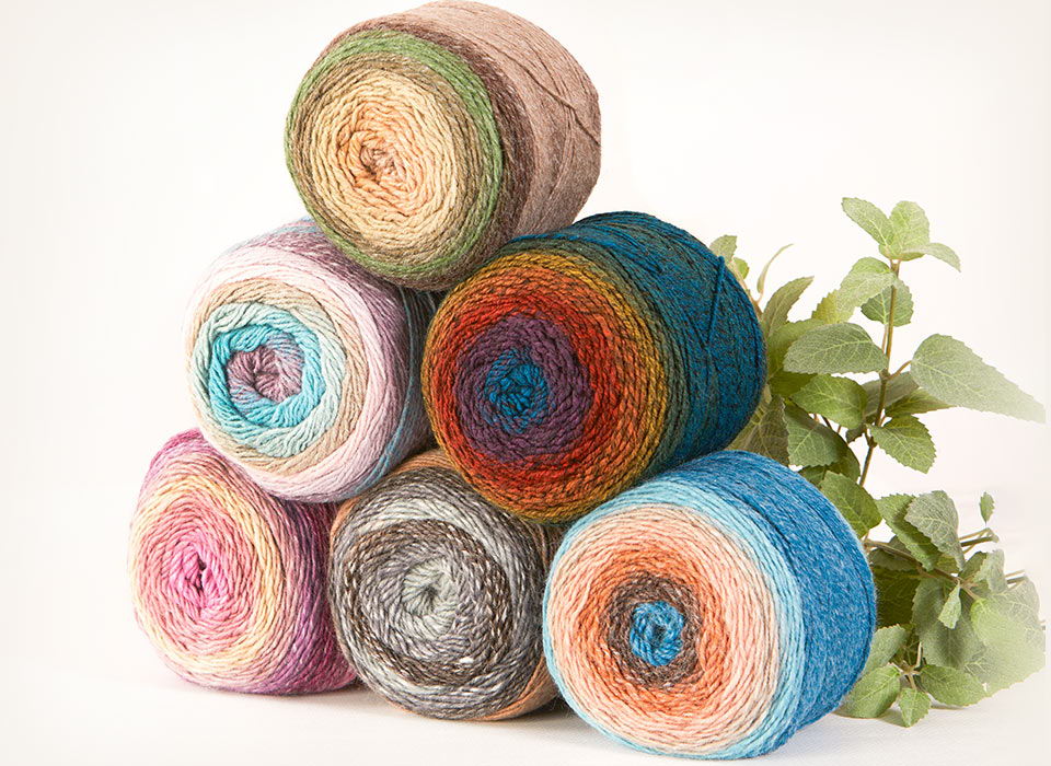 Colorful yarn cakes stacked with a green plant beside them.