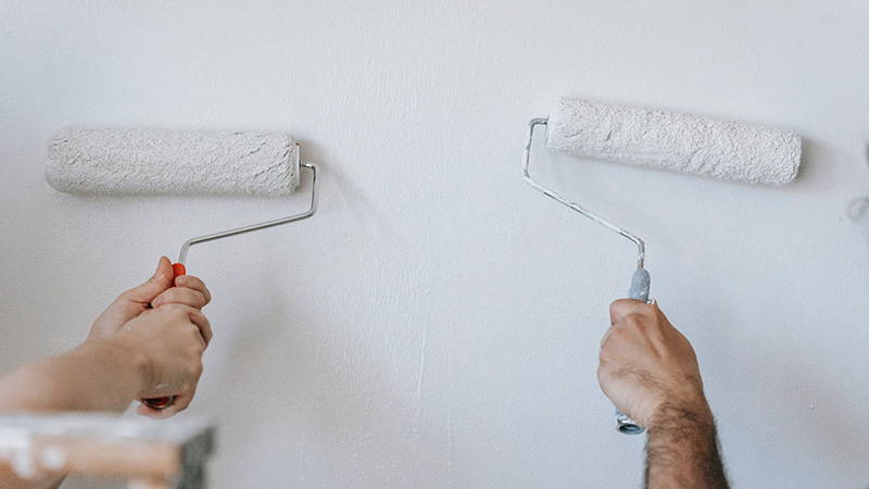 Two hand rollers painting a wall