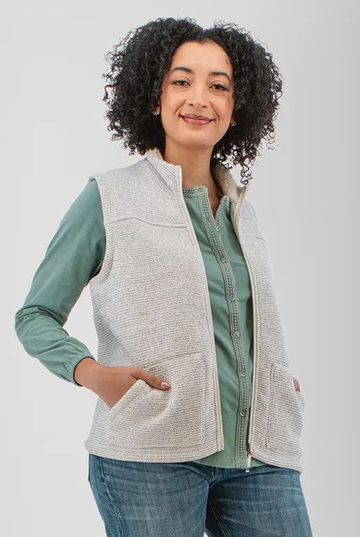 Smiling woman wearing a light vest over a green shirt, hands in pockets.