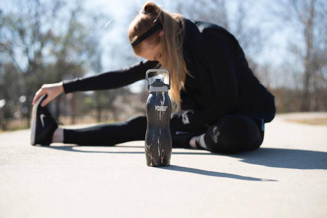 A woman stretching on a sidewalk with her Healthy Human Curve water bottle