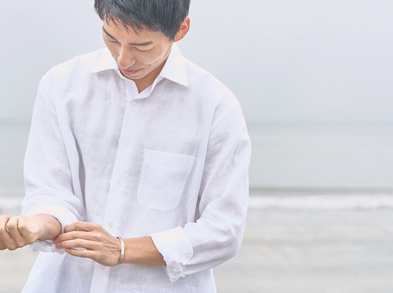 A man adjusting his sleeve near the ocean.