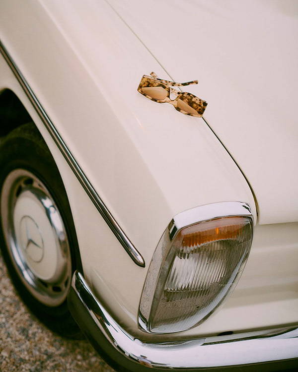 The Alex sunglasses in Coquina sat on the hood of a vintage car.