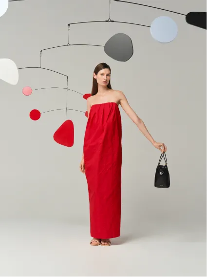 Model in a red strapless dress holding a black handbag.