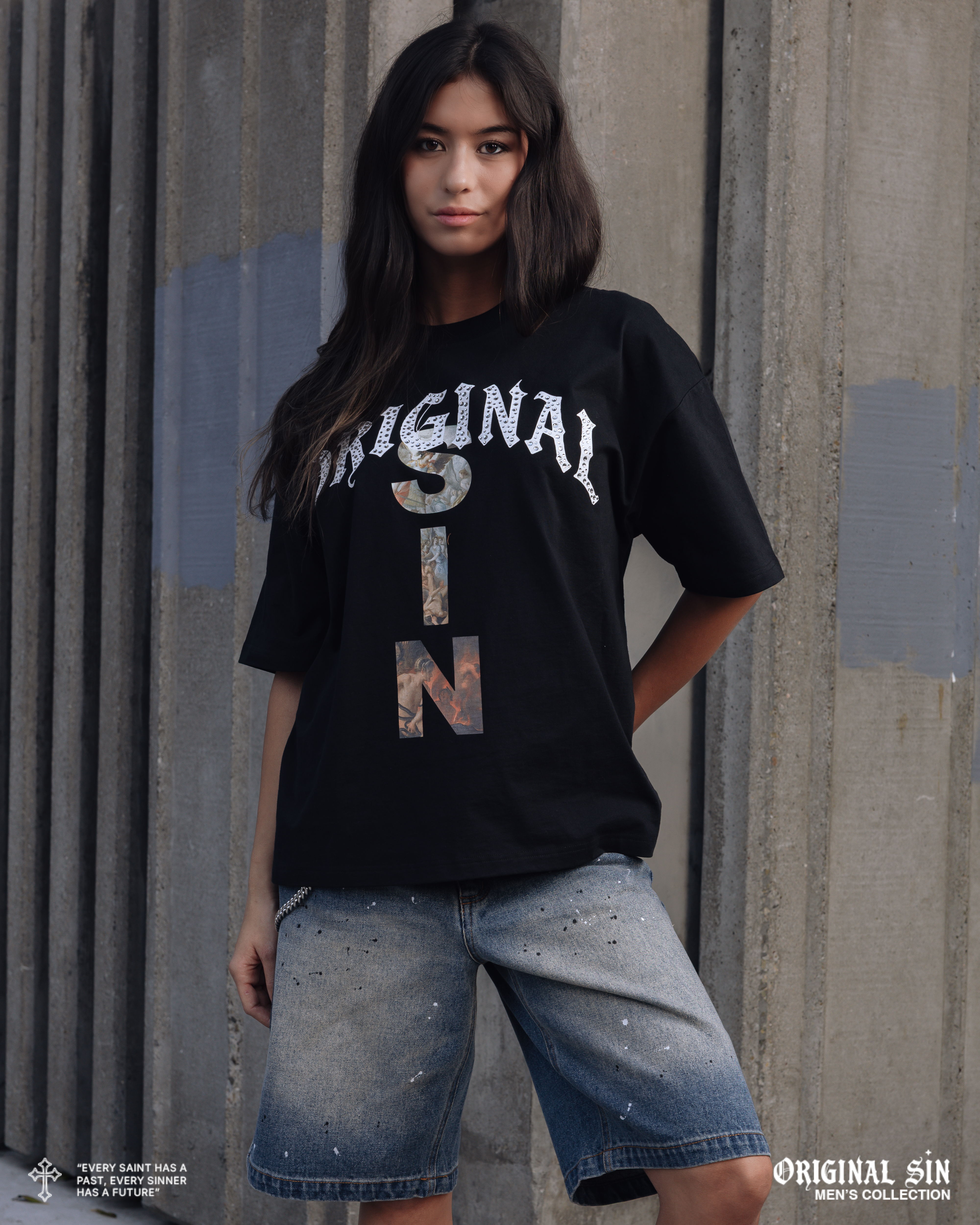 Young woman in a black t-shirt and denim shorts posing outdoors.