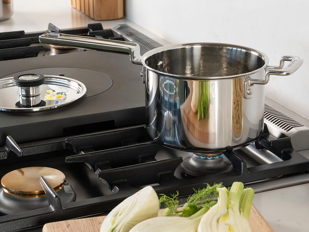 316 Series stainless-steel saucepan on a gas stove with vegetables nearby.
