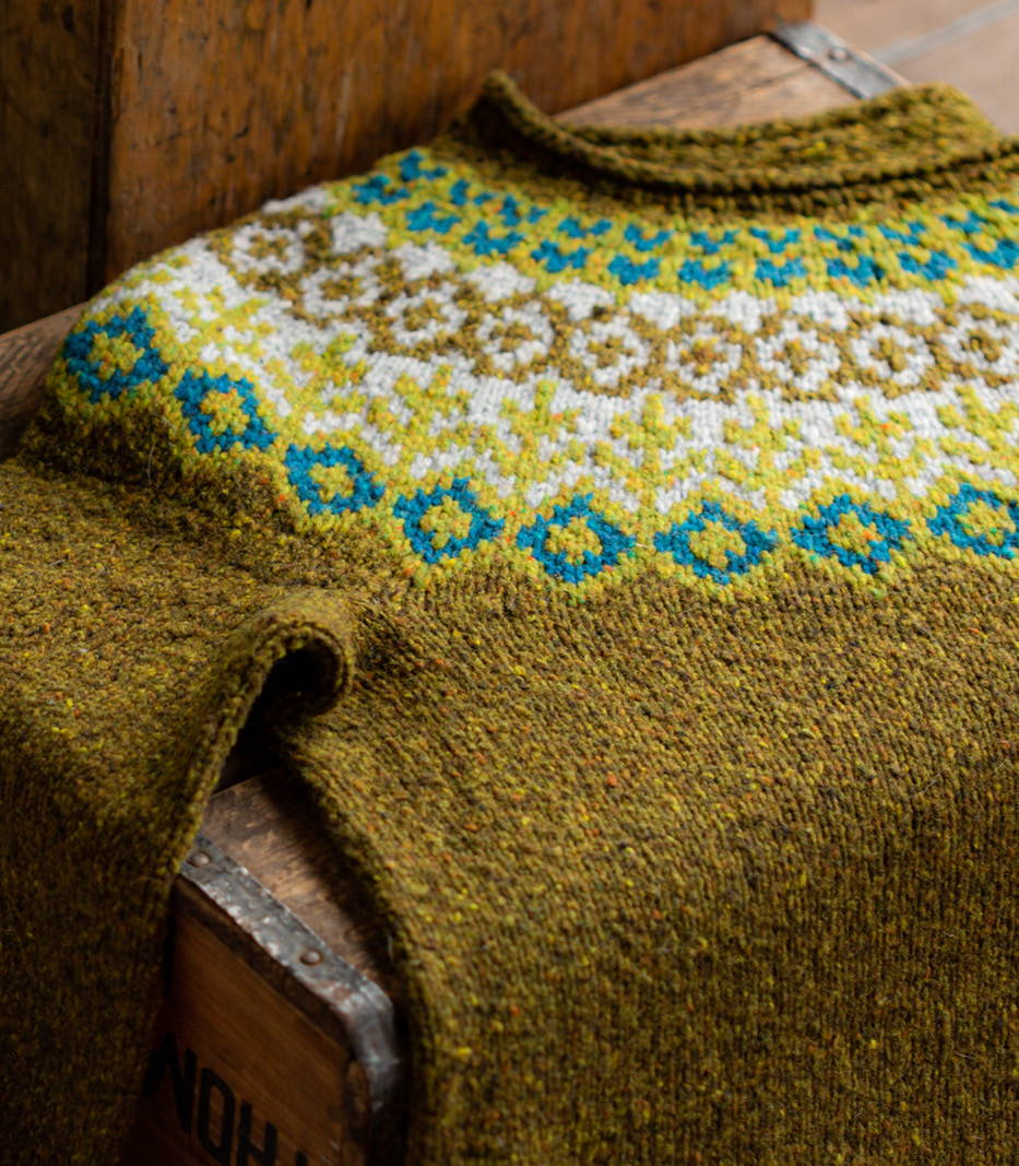 An Icelandic-style colorwork yoke hand knit pullover lies on a wooden box.