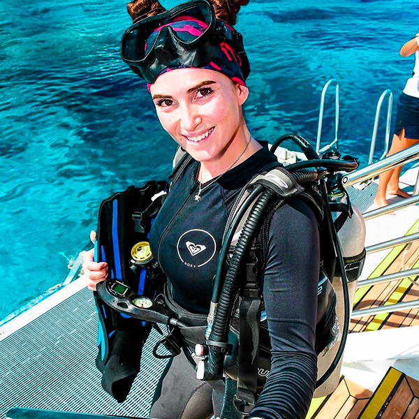 Sally Higgs, on a boat, smiling at the camera wearing scuba gear and a face shield as a headband.