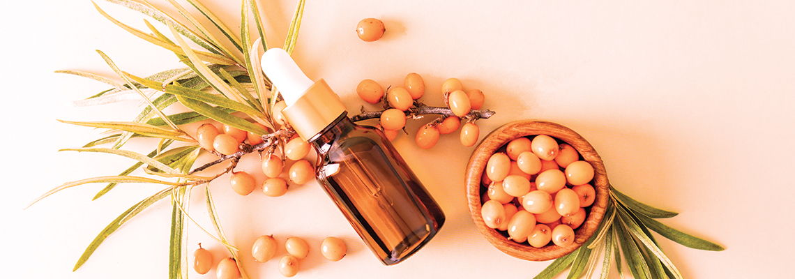 Brown bottle with lid beside a bowl of orange berries and green leaves.