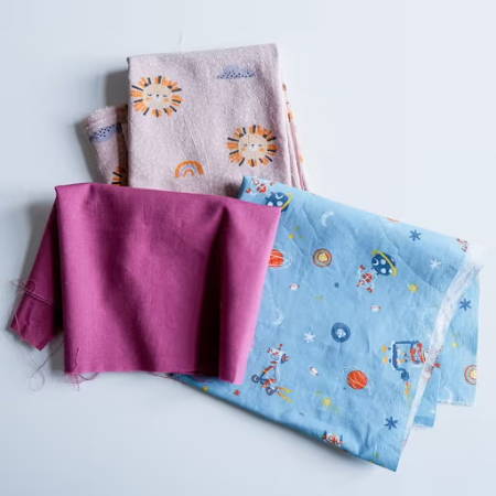 three different cotton fabrics, one plain fuchsia and two with colorful prints for kids
