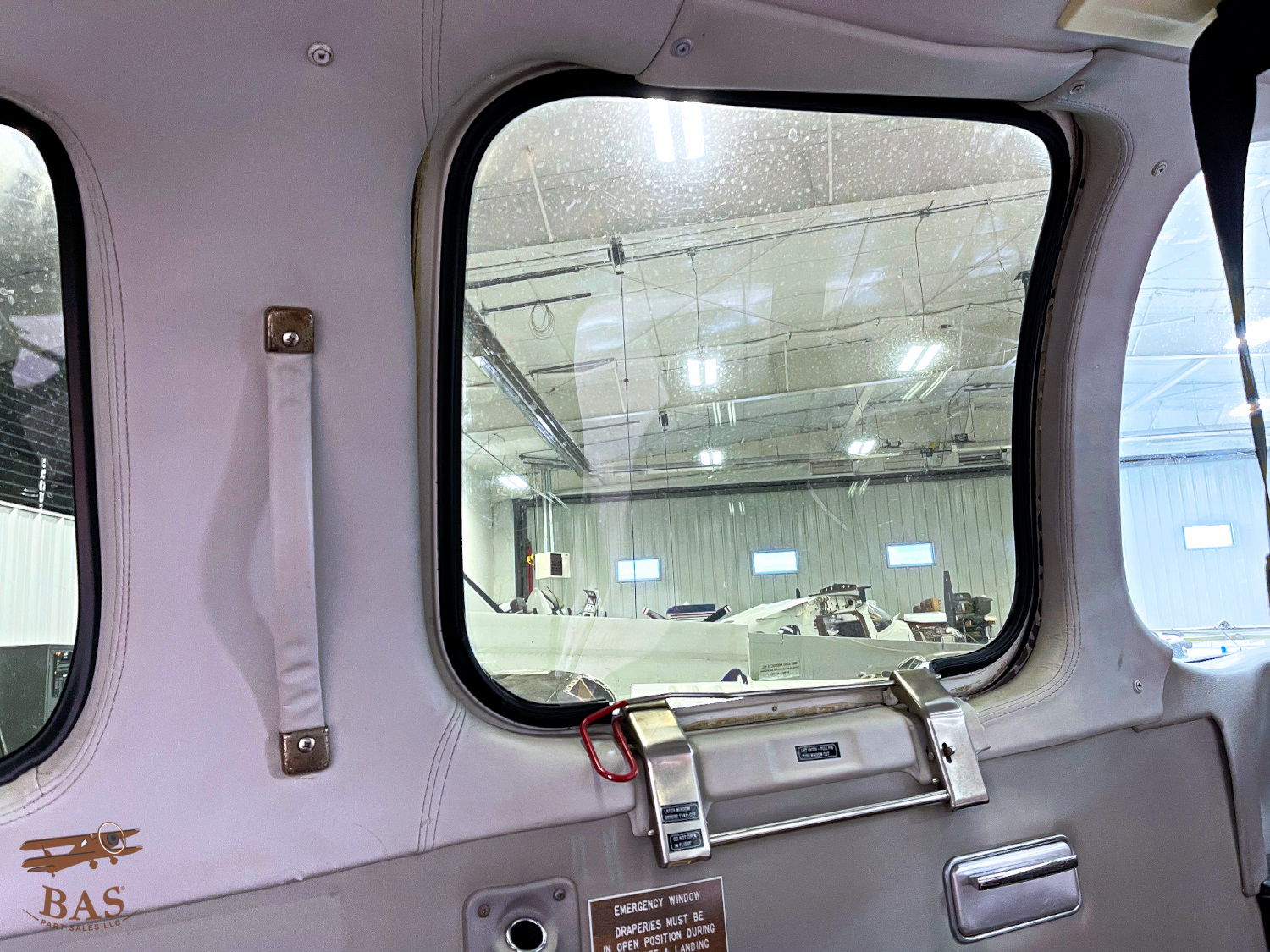 Interior view of an aircraft window looking into a hangar.