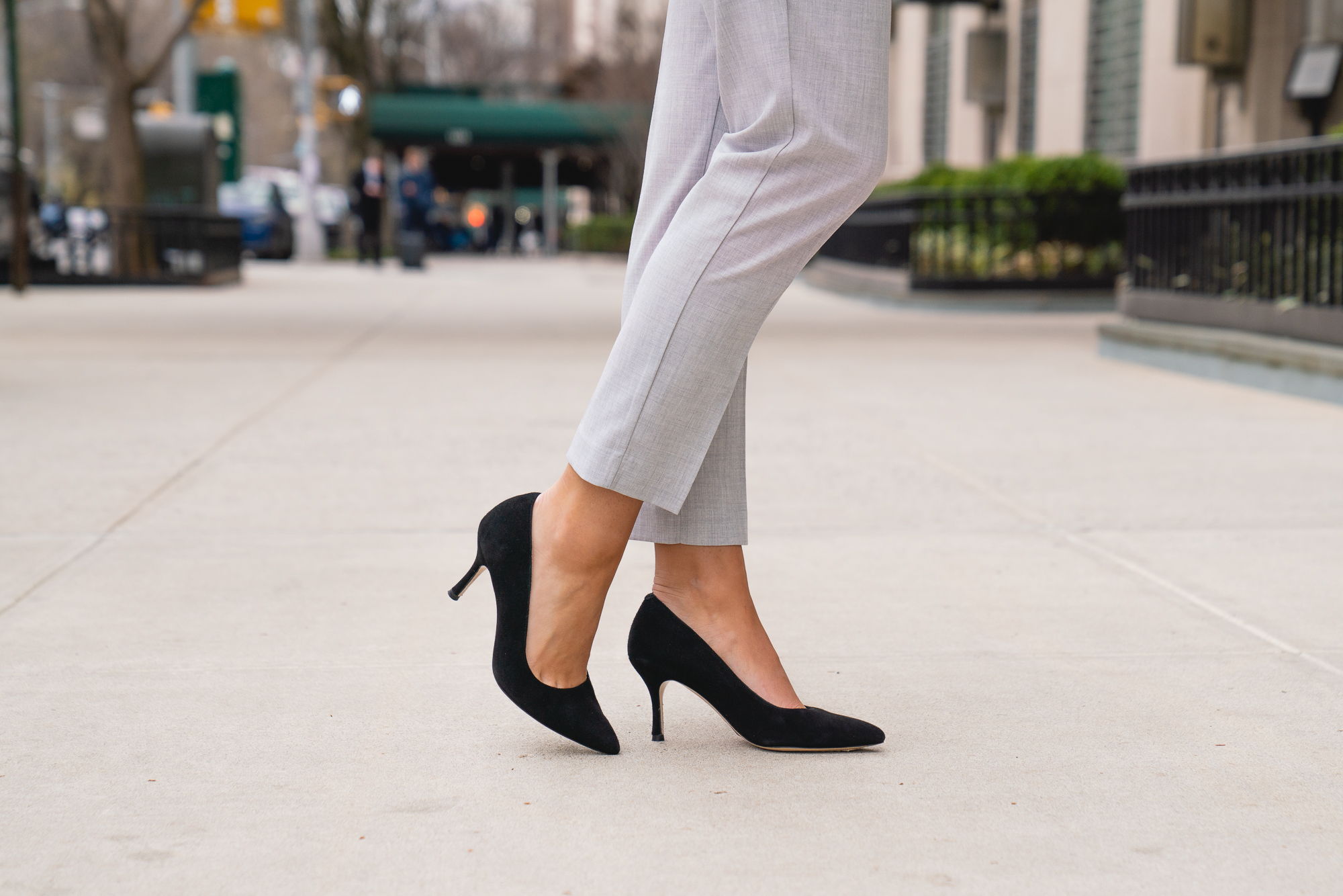 Person wearing black high heels on a city sidewalk.