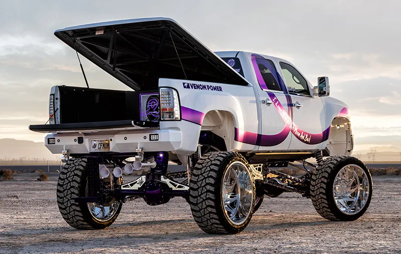 Rear three-quarter view of lifted white GMC truck with open bed cover
