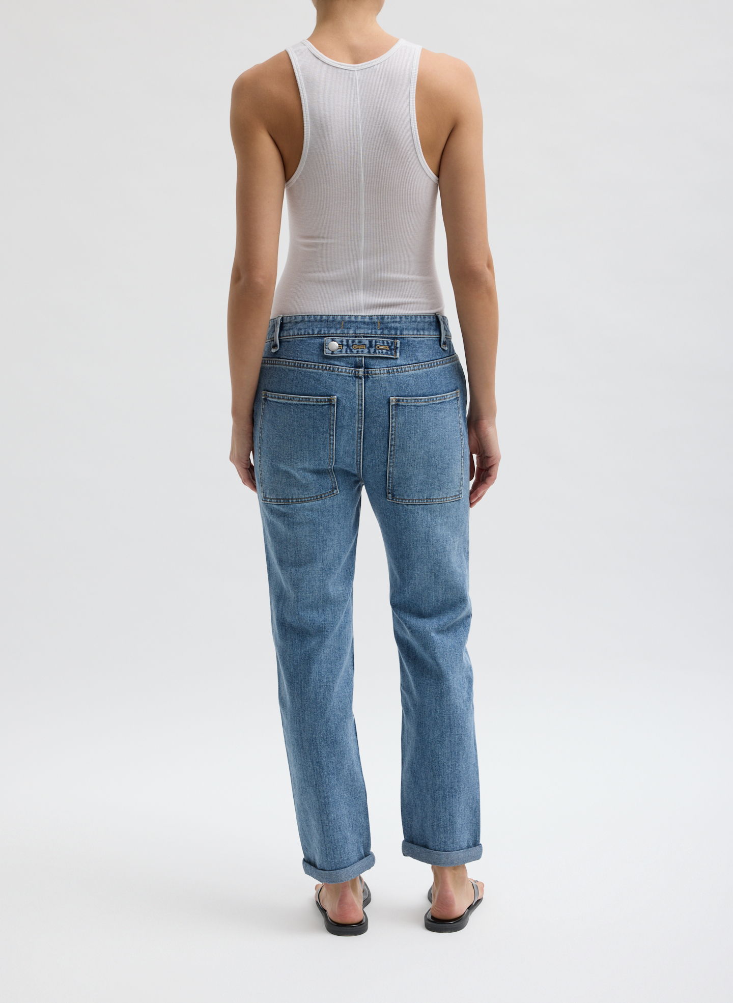 Person wearing a white tank top and blue jeans, viewed from behind.