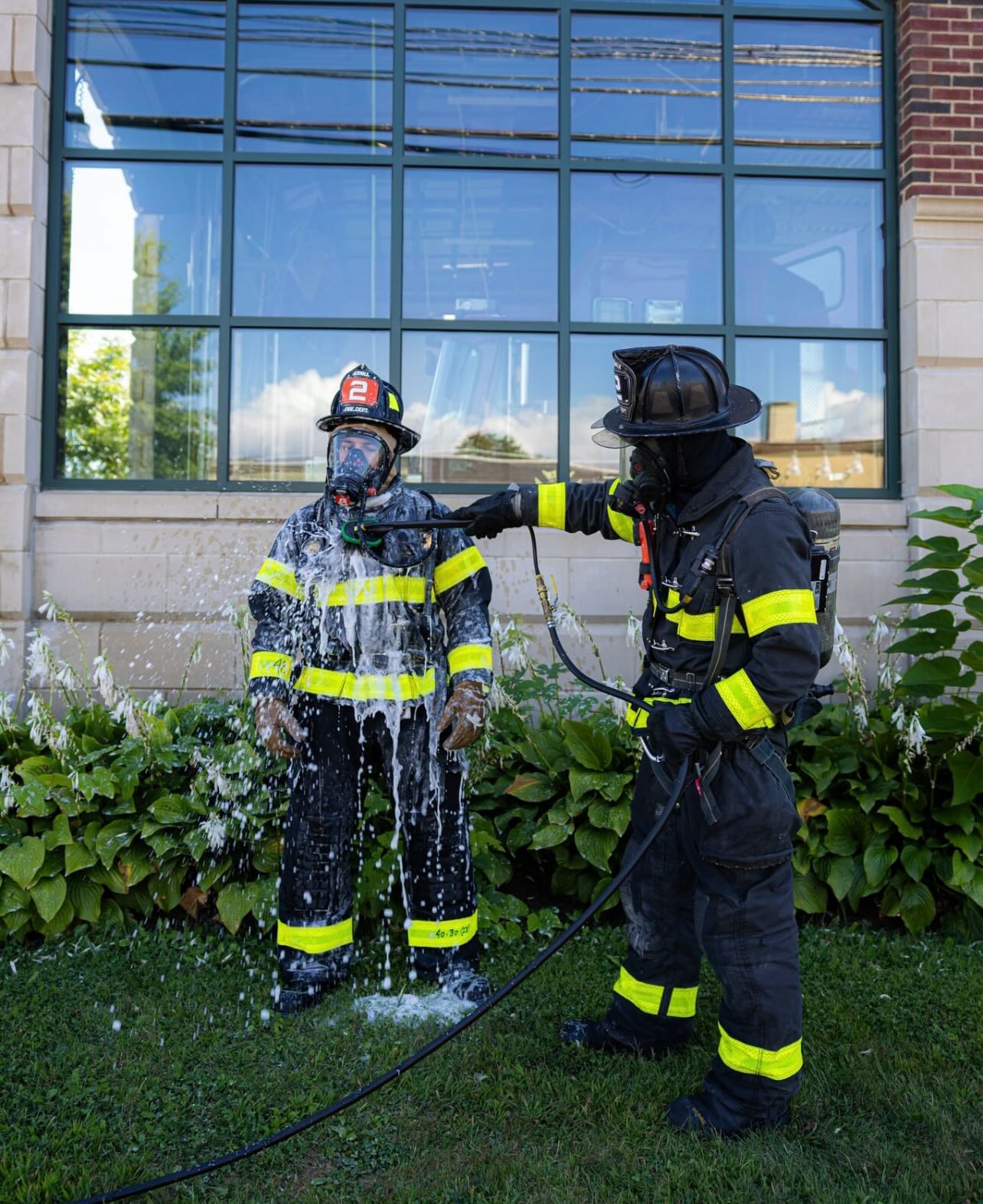 Firefighter spraying water on a training dummy in a garden setting.