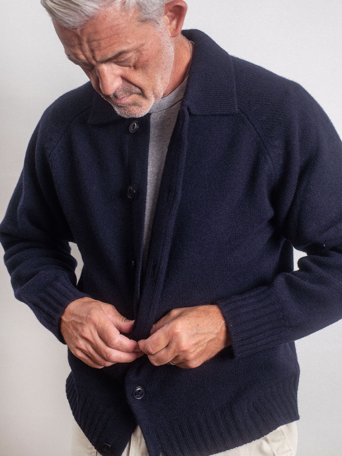 Rob buttoning a navy cardigan sweater against a neutral background.