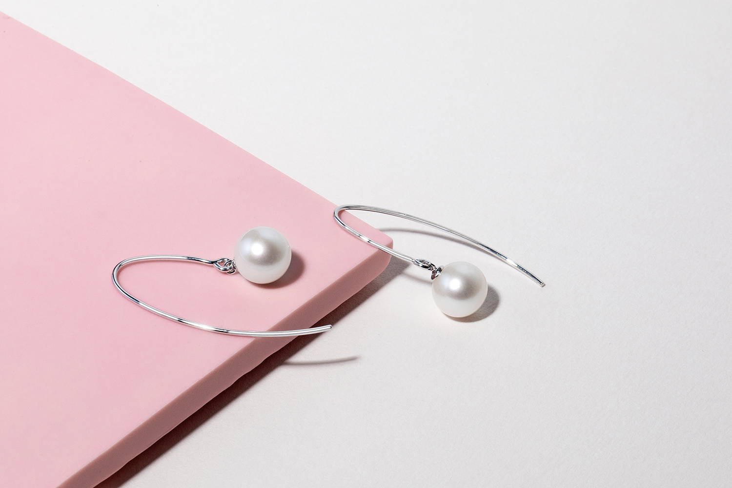White pearl dangle earrings on pink and white background