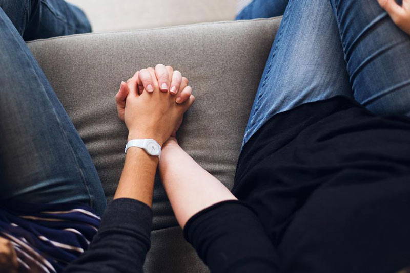 Two people sitting on a couch holding hands.