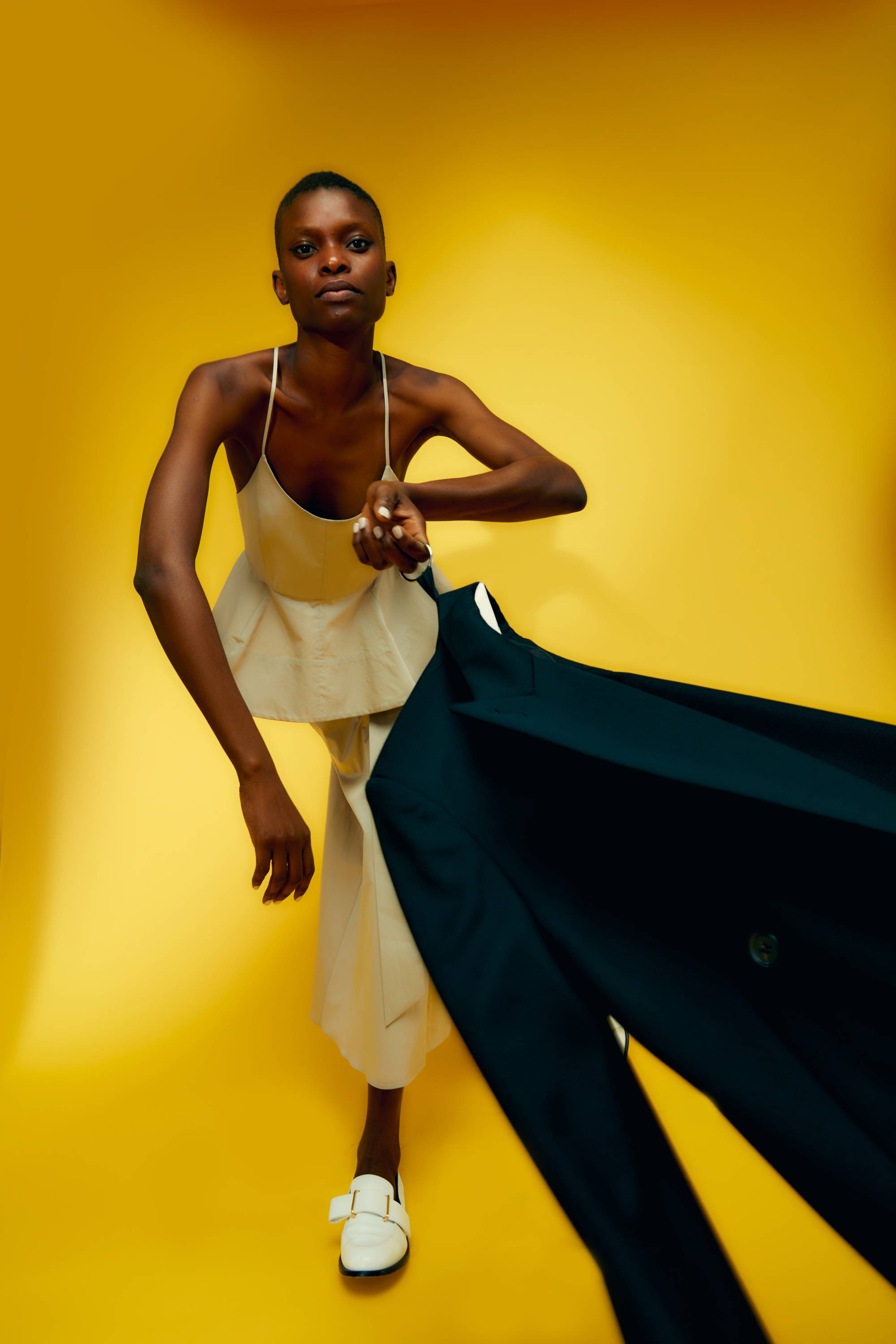 Model in a light outfit pulling a dark suit against a yellow background.