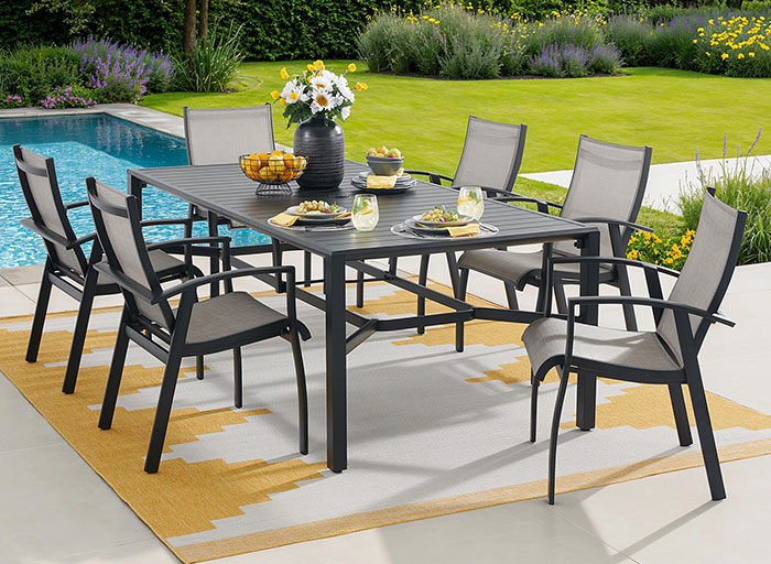 Outdoor dining table with chairs near a pool and garden.