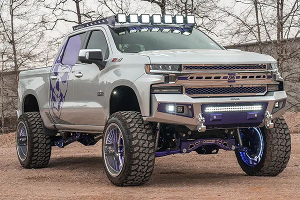 Low-angle wide view Ismael's custom lifted silver Silverado with purple accents and roof lights photo 4