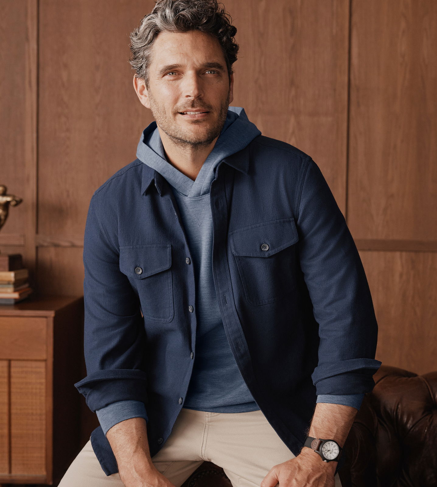 Man in a navy jacket and hoodie, sitting in a stylish interior.