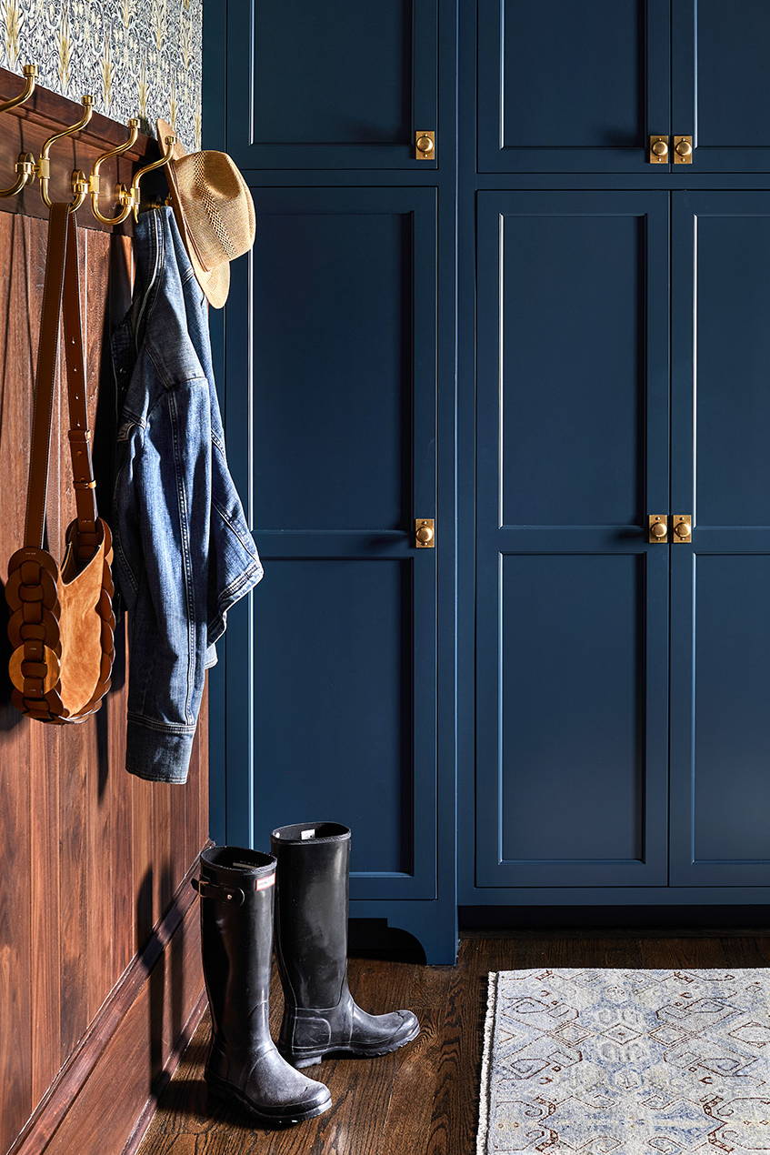 Traditional mudroom design by Elizabeth Reich Interiors with navy cabinetry, brass hardware, wood panelling, floral wallpaper, and wooden flooring
