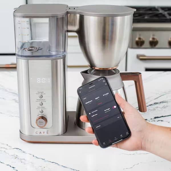 hand holding phone in front of stainless café coffee maker showing smartHQ app