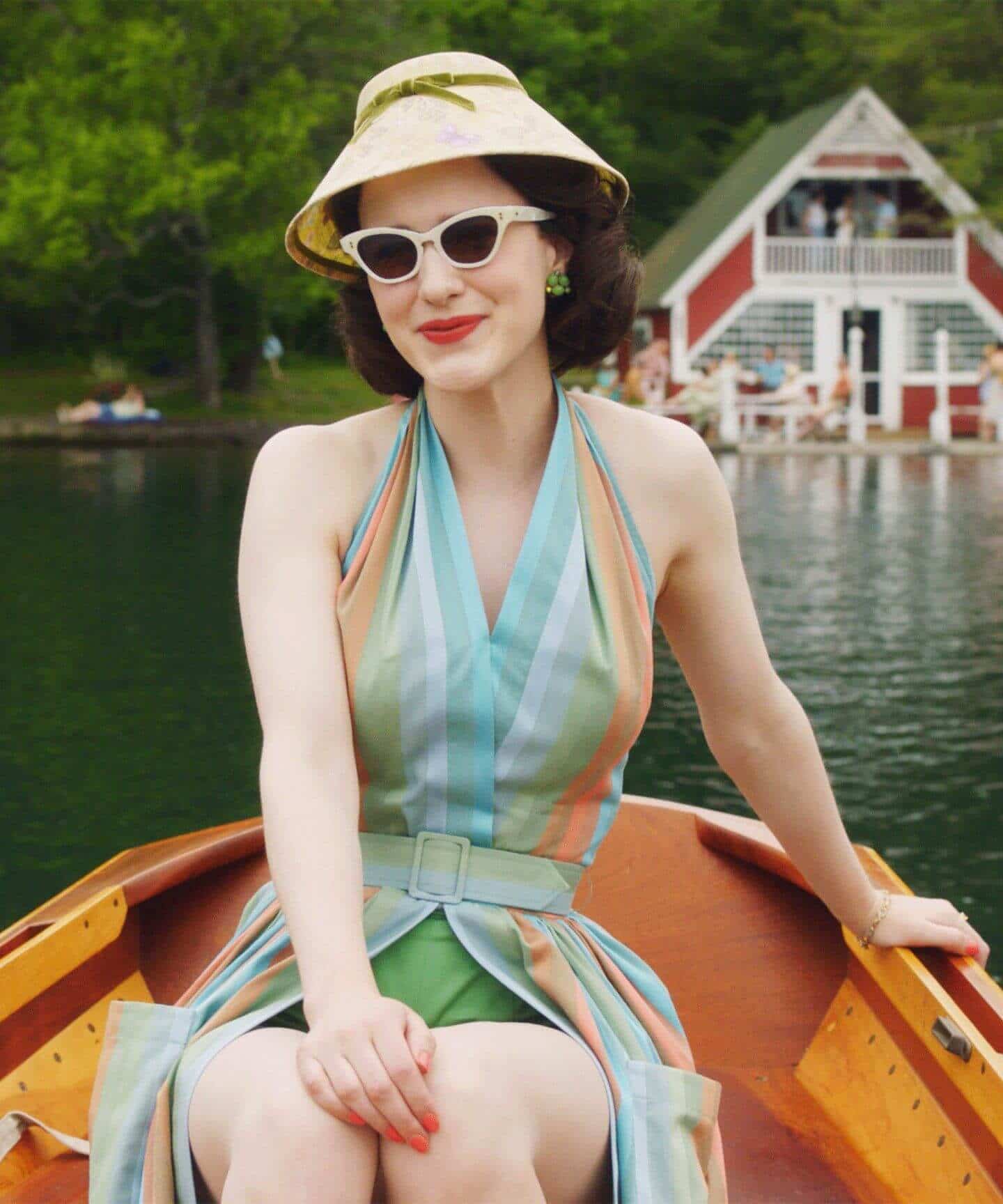 Rachel Brosnahan porte des lunettes de soleil œil-de-chat audacieuses dans La Merveilleuse Mme Maisel avec un chapeau blanc et une robe colorée