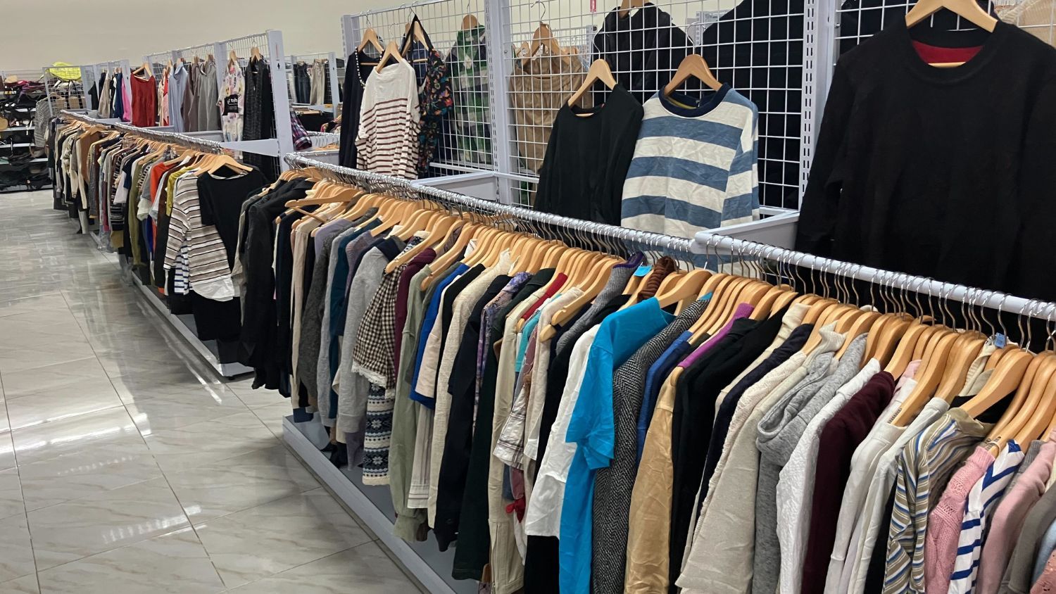 A clothing rack displaying various shirts and sweaters in a store.