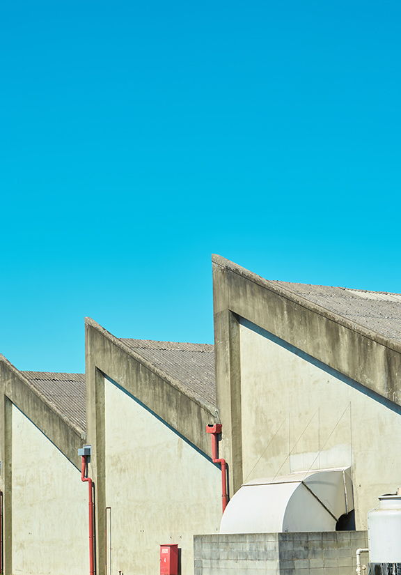 Industrial buildings with angular roofs against a clear blue sky.