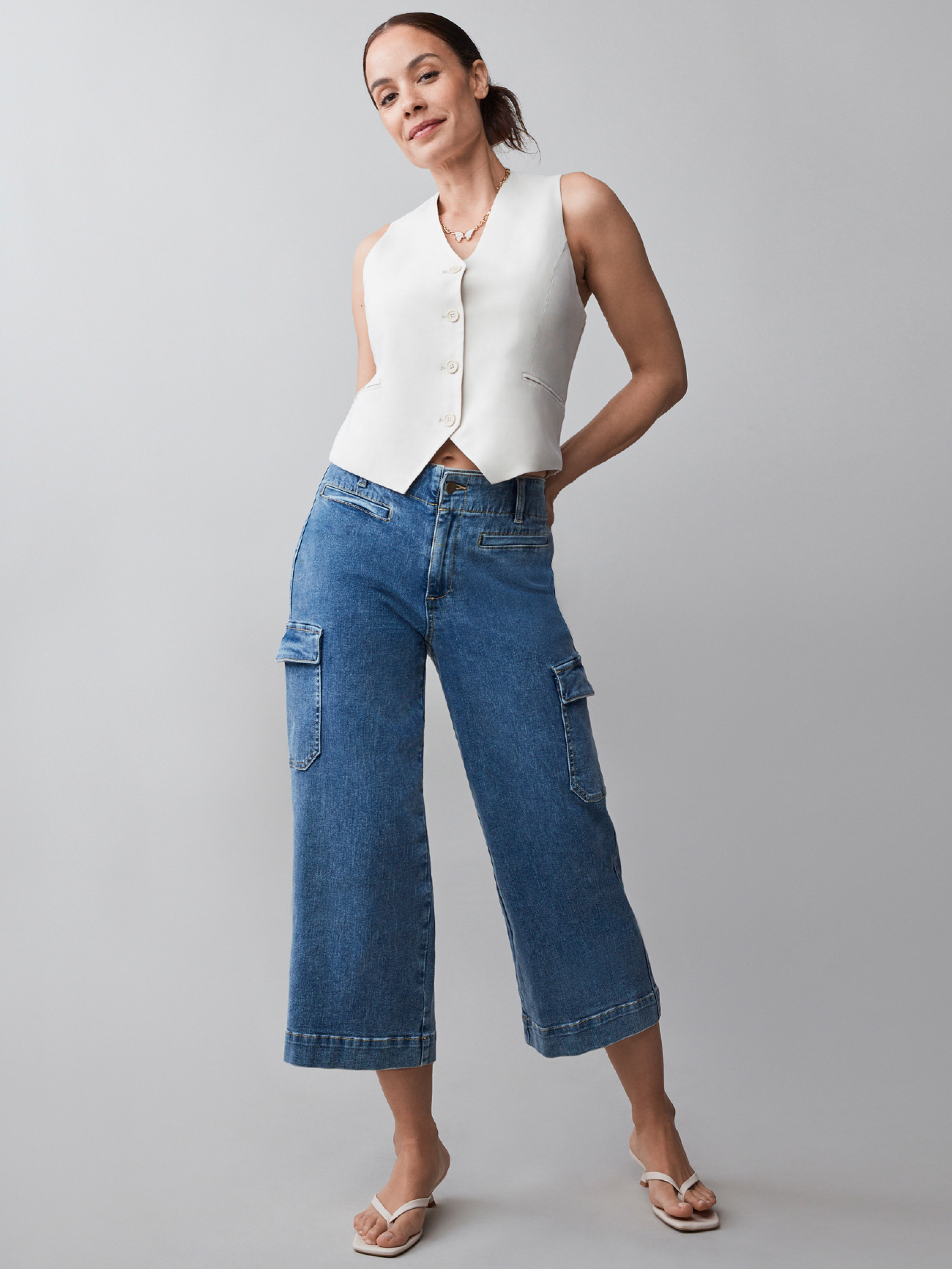 Model wearing a white vest and blue wide-leg jeans, posing confidently.