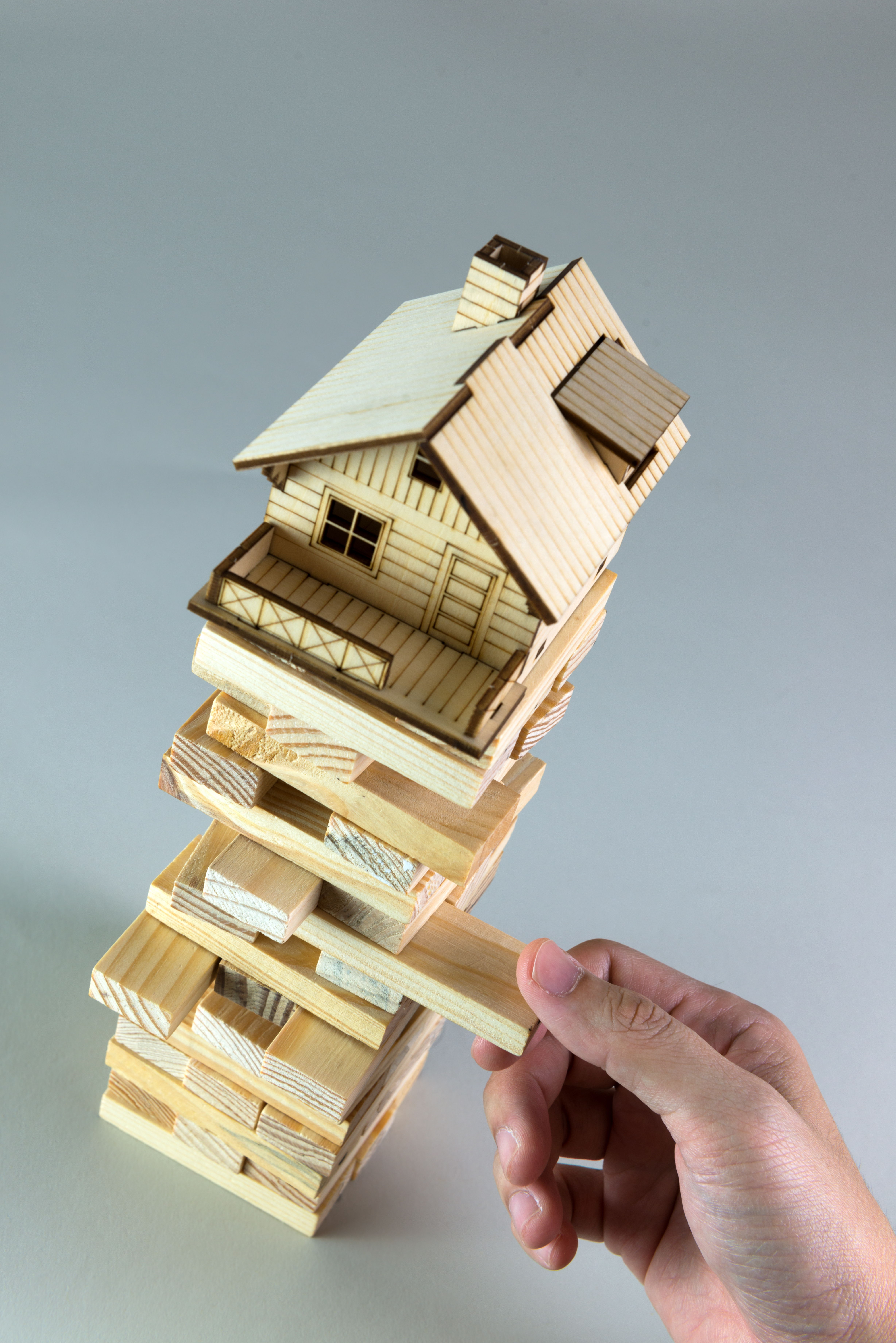 A hand removing a block from a wooden stacking game with a house on top.